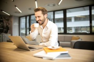 Depth of Field Photo of Man Sitting on Chair While Holding Cup in Front of Table